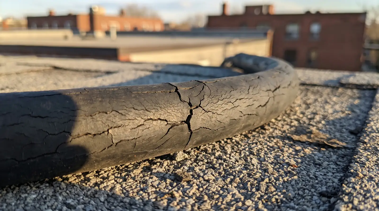 Close-up of a cable whose black jacket is cracked all over, lying on a gravel flat roof